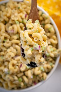 a wooden spoon full of macaroni salad on top of a white bowl with an orange in the background