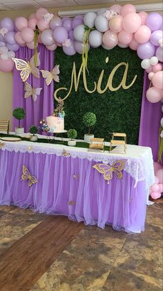 a table with purple tulle skirt and gold butterfly decorations on it, surrounded by balloons