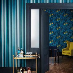 a room with blue and green wallpaper, yellow chairs and a gold bar cart