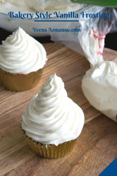 three cupcakes with white frosting sitting on a cutting board next to a plastic bag