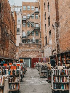 an alleyway filled with lots of books in front of tall buildings and brick walls