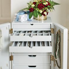 a white cabinet with many drawers and flowers on the top one drawer is open to show jewelry