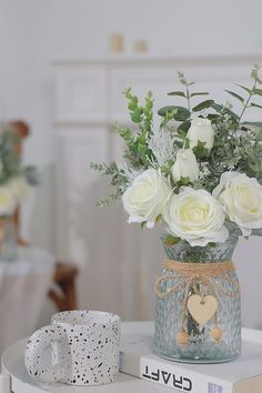 a vase with white flowers on top of a table next to a book and mug