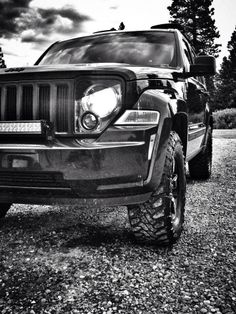 a black and white photo of the front end of a truck parked on gravel with trees in the background