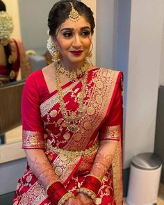 a woman in a red and gold bridal outfit sitting on a chair with her hands clasped to her chest