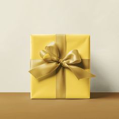 a yellow gift box with a gold bow on the top, sitting on a table