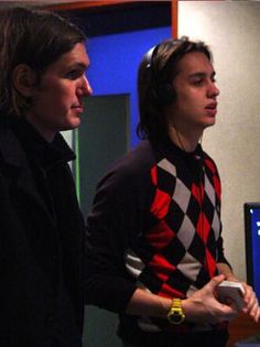 two young men standing next to each other in front of a computer monitor and keyboard