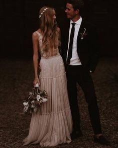 a man and woman standing next to each other in front of a dark background holding flowers