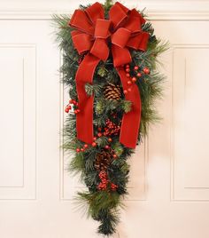 a christmas wreath with pine cones and red bows hanging on the front door or wall