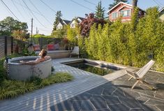 a woman relaxing in an outdoor jacuzzi tub next to a deck and garden