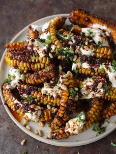 a white plate topped with grilled corn covered in ranch dressing