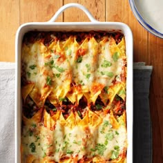 a casserole dish with cheese and vegetables in it on a wooden table next to a plate