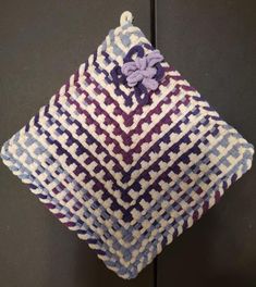 a close up of a knitted pillow on a black surface with purple and white designs