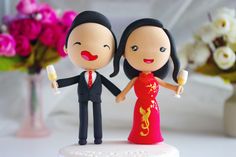 a bride and groom figurine holding hands on top of a table with flowers in the background