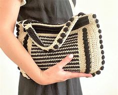 a woman is holding a crocheted purse in her left hand while wearing a black and white dress