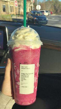 a person is holding up a drink in their hand while driving down the street with cars behind them