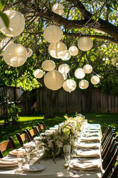 a long table with paper lanterns hanging from it's branches and place settings on the table