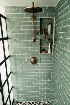 a bathroom with green tile and gold faucet in the shower head, hand held soap dispenser on the wall