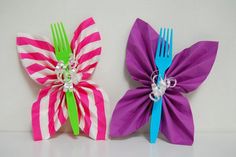 two colorful paper flowers are sitting side by side on a white surface, one is purple and the other is green