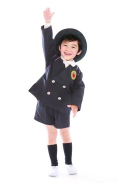 a little boy dressed in a uniform and hat is raising his hand up to the sky