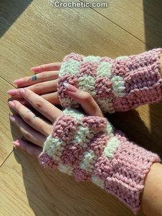 two hands with pink and white crocheted gloves on top of a wooden table