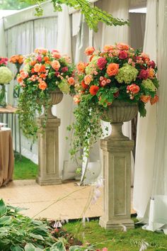 two tall vases with flowers in them sitting on the ground