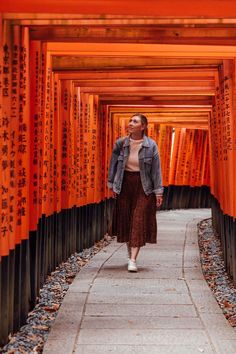 a woman walking down a path lined with orange tori toris in the distance,