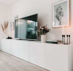 a flat screen tv sitting on top of a white cabinet next to a vase filled with flowers