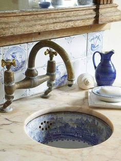 a sink in a bathroom with blue and white tiles on the wall behind it, next to an old faucet