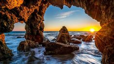 the sun is setting behind some rocks in the ocean with waves coming up on them