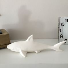 a white shark figurine sitting on top of a table next to a clock