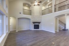 an empty living room with hard wood floors and stone fireplace in the center, surrounded by two balconies