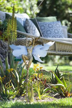 an angel statue in the middle of some plants and flowers on the ground near a couch