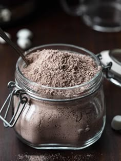 a glass jar filled with brown powder on top of a wooden table next to spoons