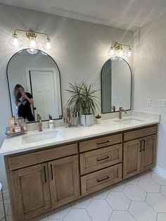 a woman takes a photo of her bathroom vanity with two mirrors and lights above it