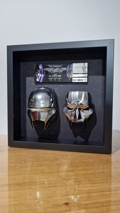 two silver helmets are in a black shadow box