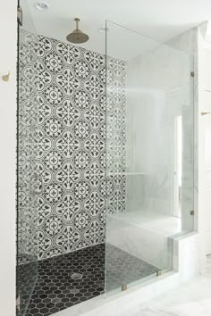 a bathroom with black and white tiles on the shower wall, glass door to the bathtub