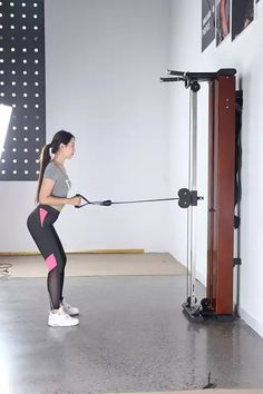 a woman is doing pull ups with a resistance rope in a gym area, while another person watches from the side