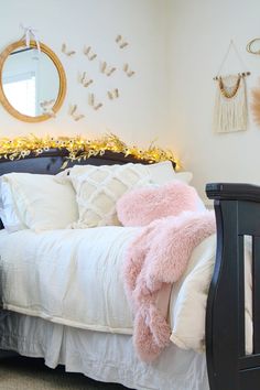 a bed with white sheets and pink fluffy pillows on it, next to a mirror