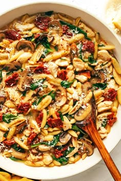 a white bowl filled with pasta and spinach covered in sauce next to some bread