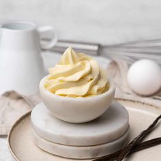 a white bowl filled with whipped cream sitting on top of a plate next to eggs