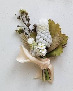 a boutonniere with white flowers and green leaves on a table next to the wall