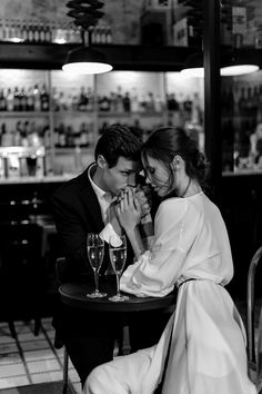 a man and woman sitting at a table in front of each other with wine glasses