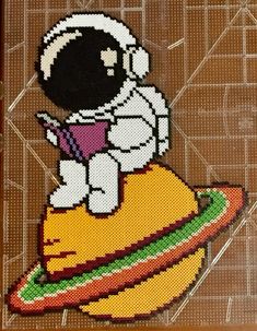 a cross stitch picture of an astronaut on top of a saturn rocket with the earth in the background