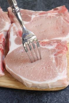 a piece of raw meat with a fork stuck in it's center, on a cutting board