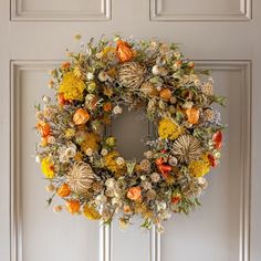 a wreath hanging on the front door of a house with orange and yellow flowers in it