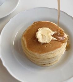 a stack of pancakes on a plate with butter and syrup being drizzled onto them