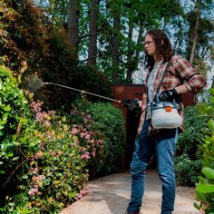 a man with a sprayer in his hand is spraying water on the ground near some bushes