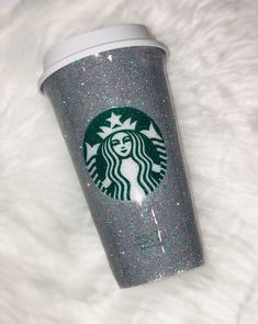 a starbucks cup with glitter on it sitting on top of a white fur covered floor