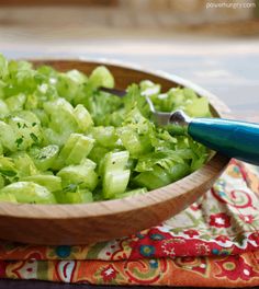 a wooden bowl filled with celery on top of a colorful cloth next to a knife